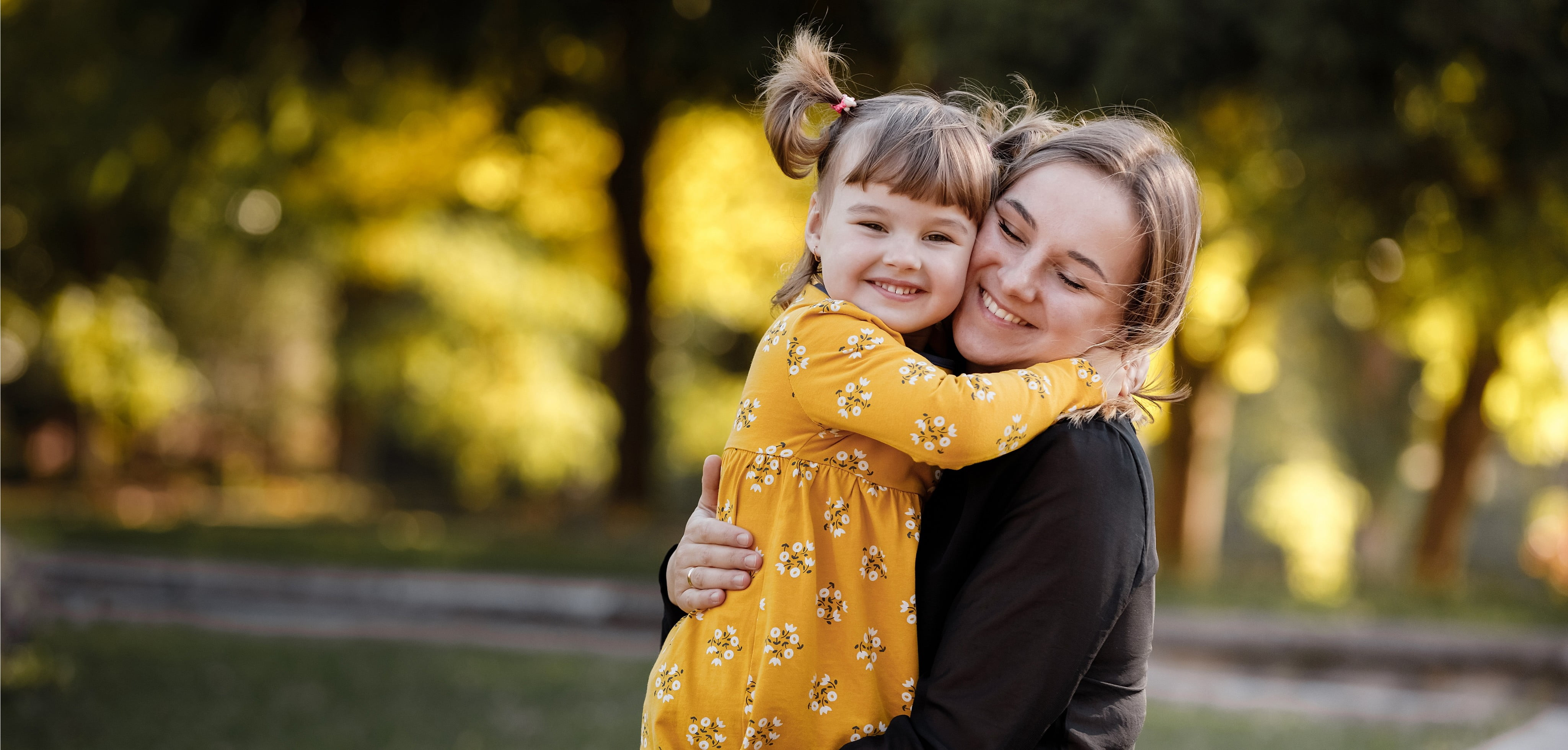 a little girl and a young lady hugging outside.