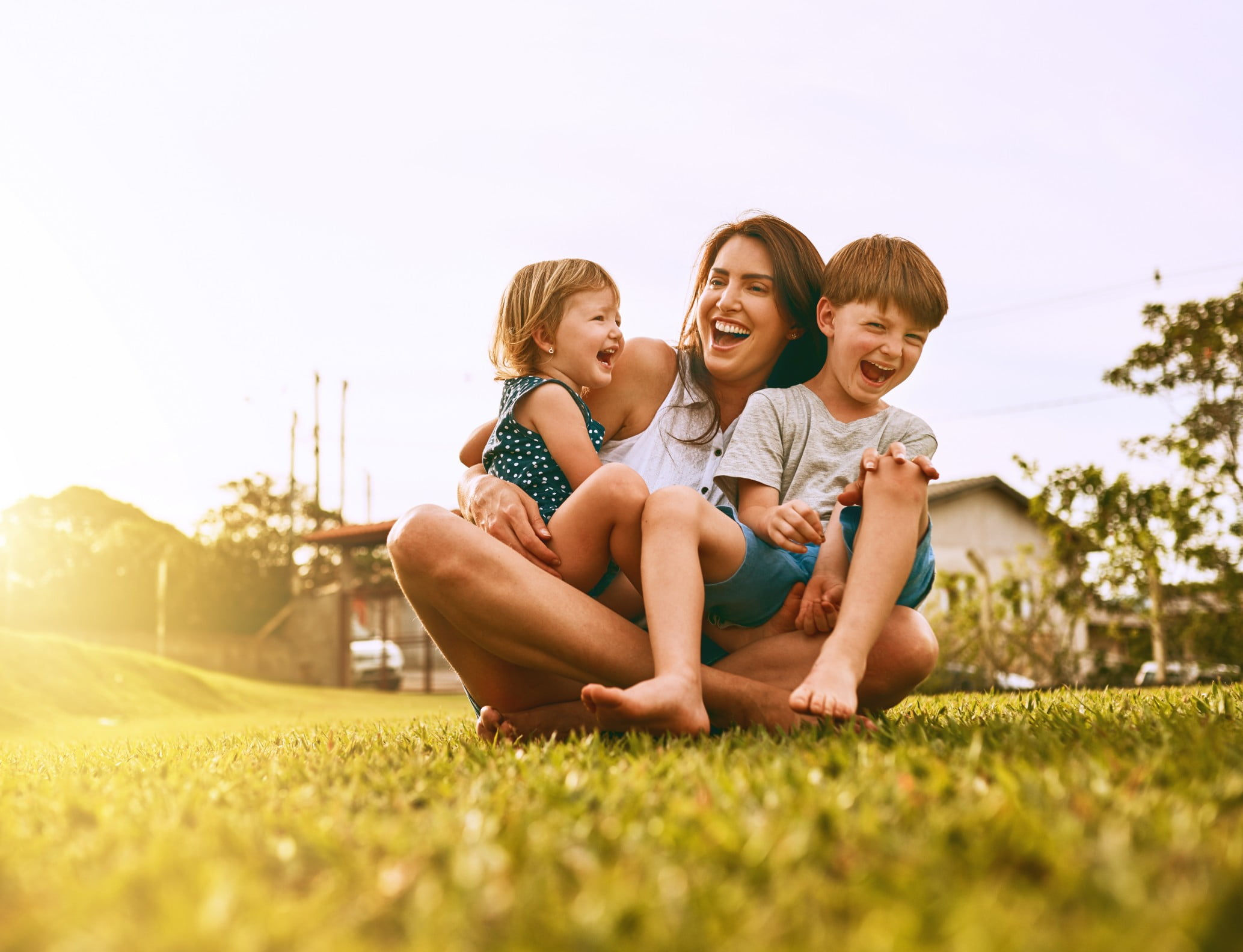 A young lady with two kids laughing outside on a lawn