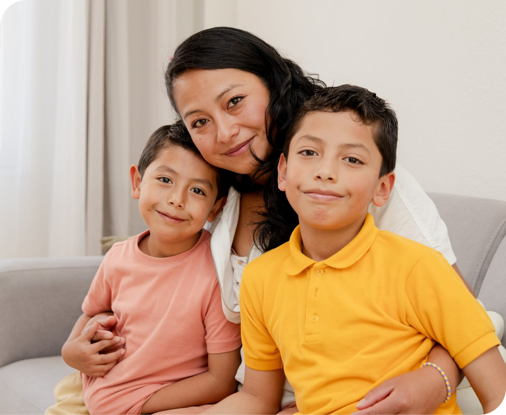 A picture of a mother and her two kids hugging and sitting on a couch.