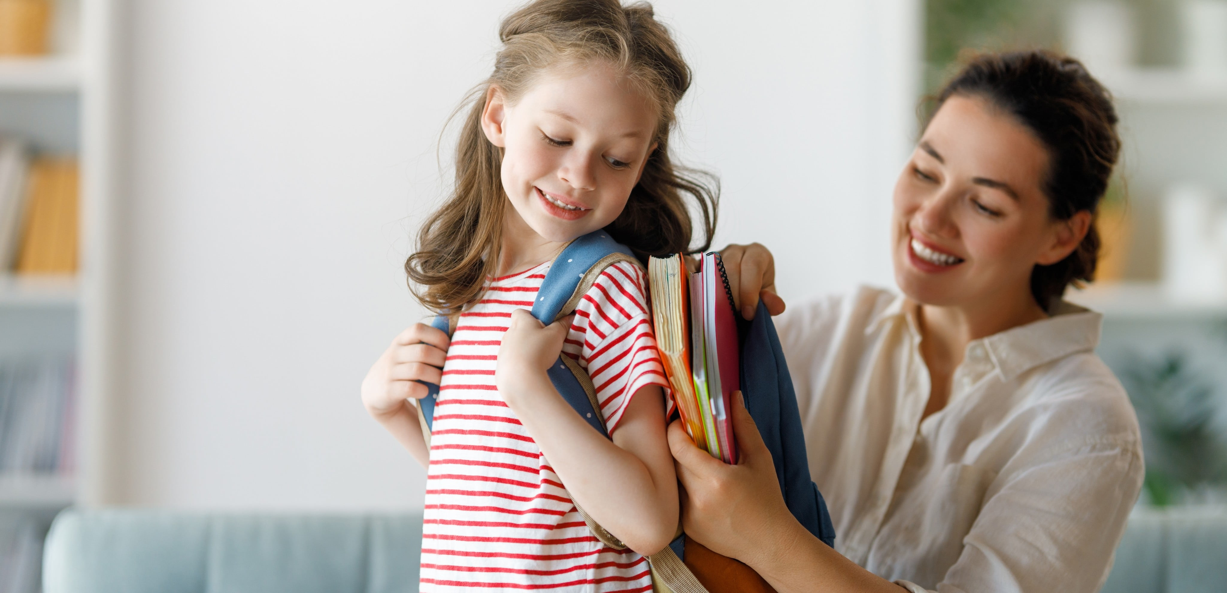 A picture of a little girl getting help with her backpack