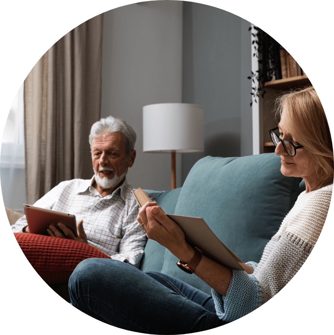 an elderly couple enjoying a quite night on the couch reading books together.