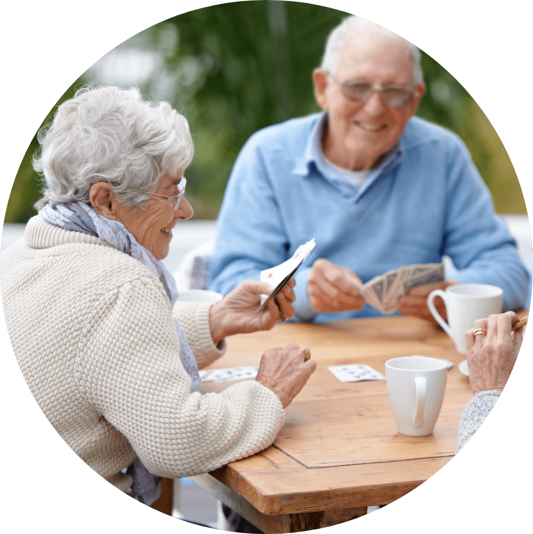 A group of elderly people laughing at a table playing cards and having coffee together.