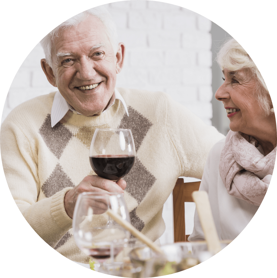 an elderly couple laughing and talking and enjoying some wine together.